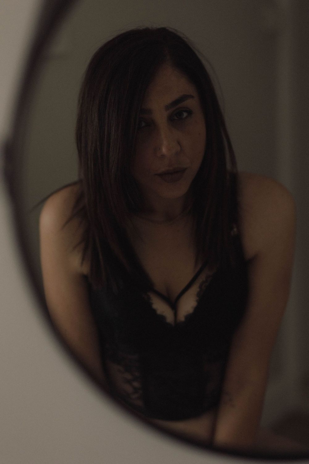 A moody mirror reflection captures a woman in black attire against a dark background.