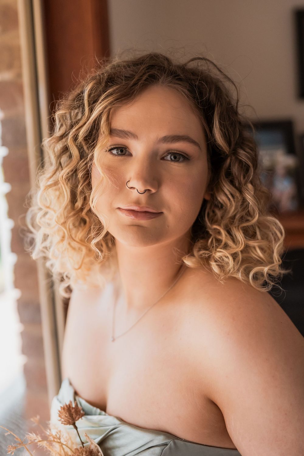 Portrait of person with curly blonde hair in soft natural light wearing an off-shoulder top.