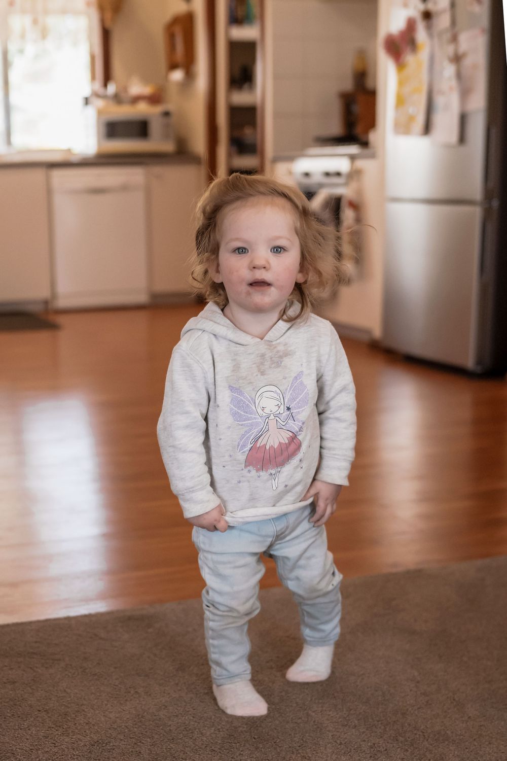 A series of four images showing a child in a light gray sweatshirt and pants standing on a carpeted floor indoors.