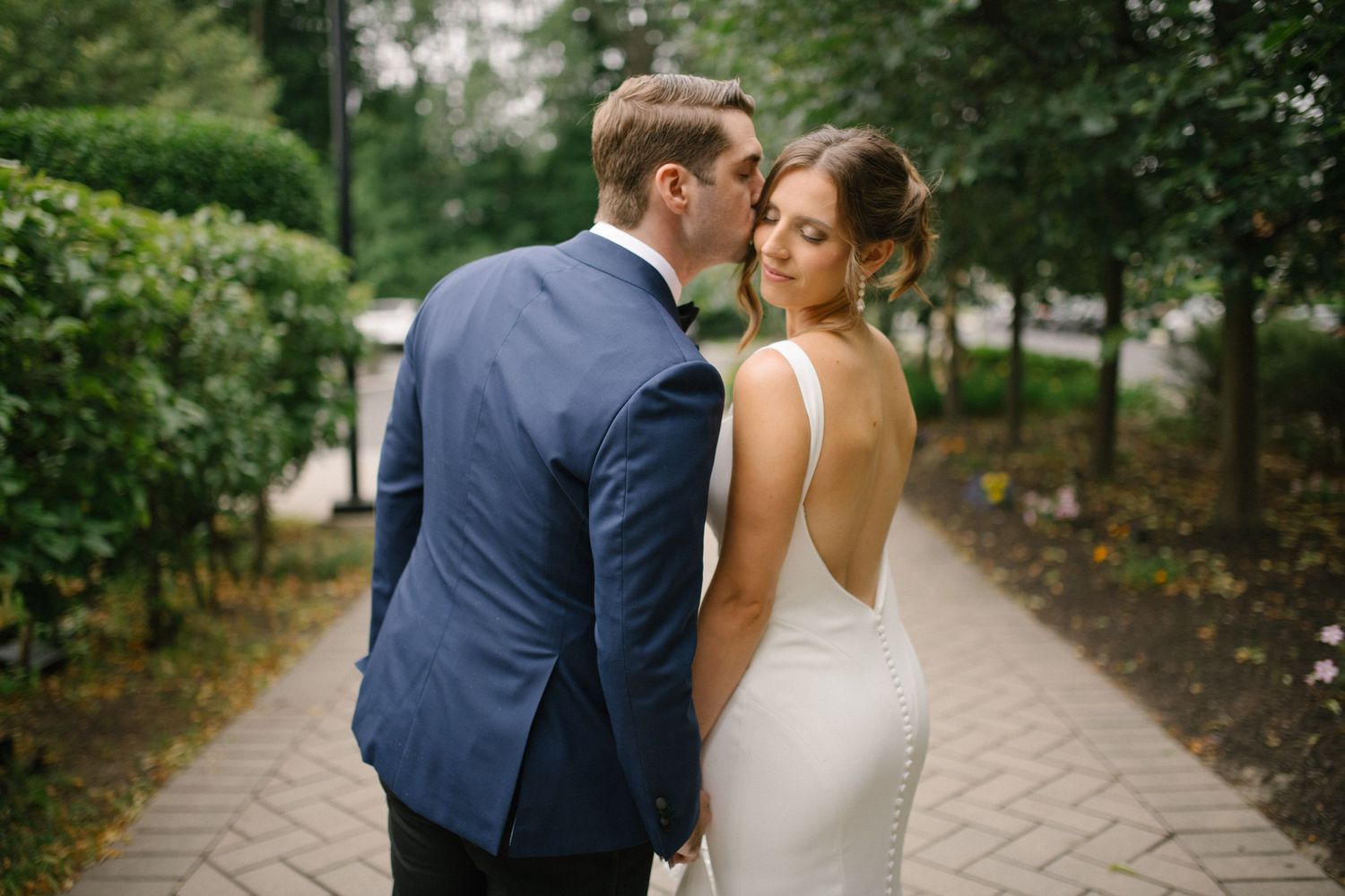 Wedding ceremony guests sit in white chairs surrounded by elegant white floral arrangements in an outdoor garden setting.
