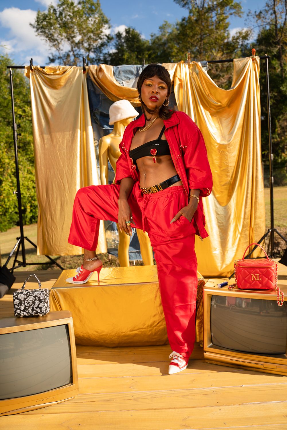 Fashion shoot featuring vibrant red outfit posed against golden fabric backdrop in natural lighting.