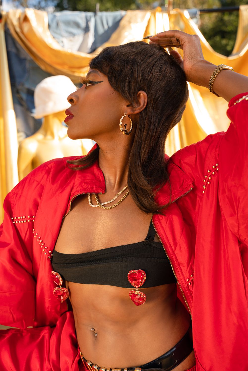 Fashion portrait of person wearing red jacket and black crop top with heart details against yellow background outdoors.