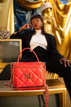 Red quilted handbag with NL monogram and chain strap displayed on gold surface with dramatic lighting.