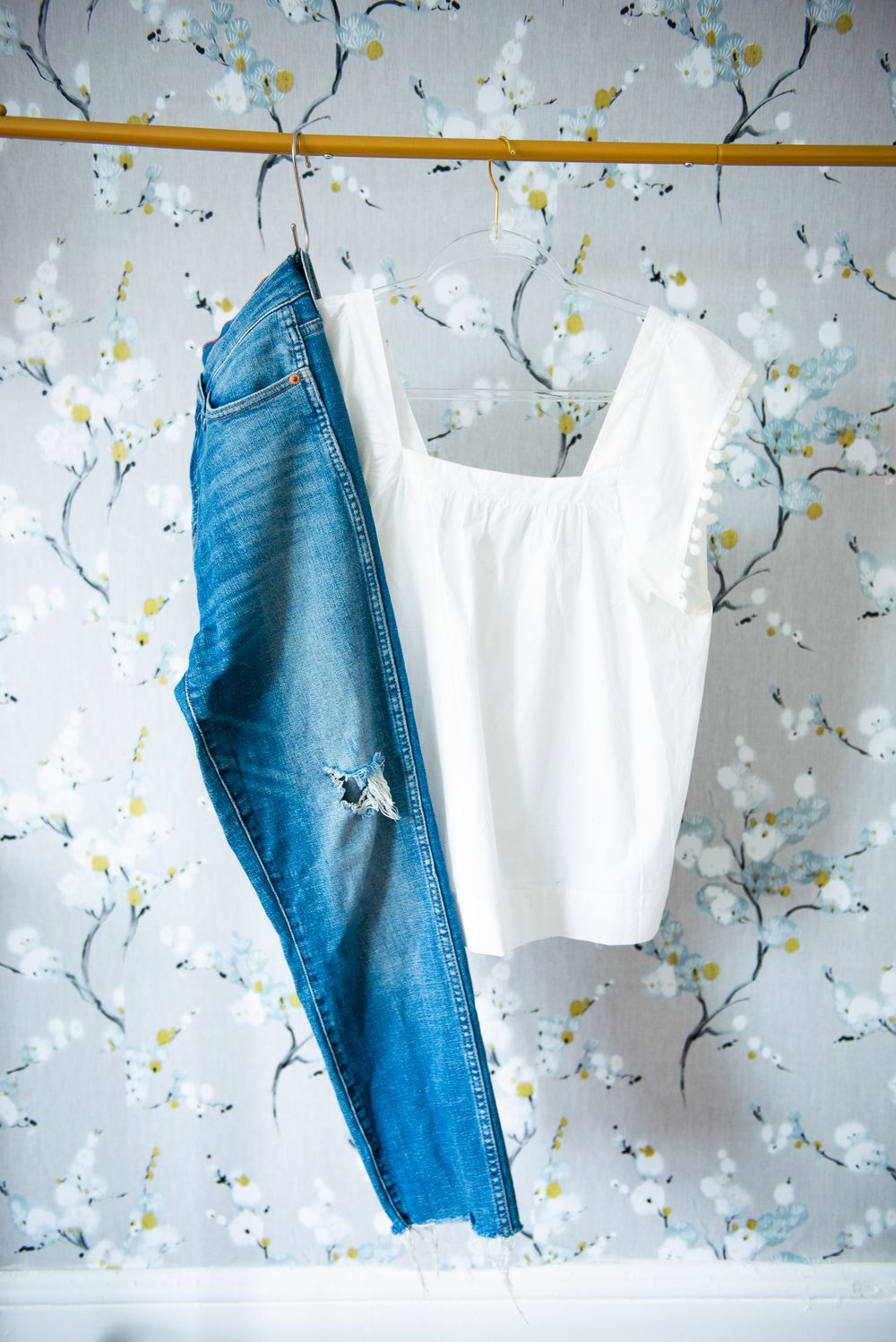 Blue distressed jeans and white sleeveless top hanging against floral wallpaper background.