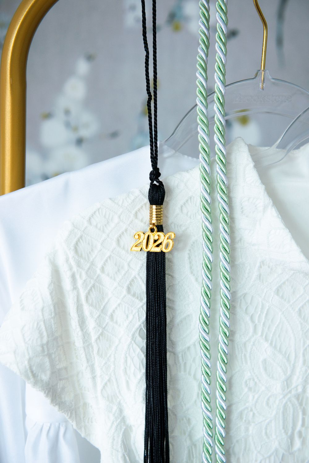 A black graduation tassel with gold 2020 charm hangs beside white garment and mint green stripes against light background.