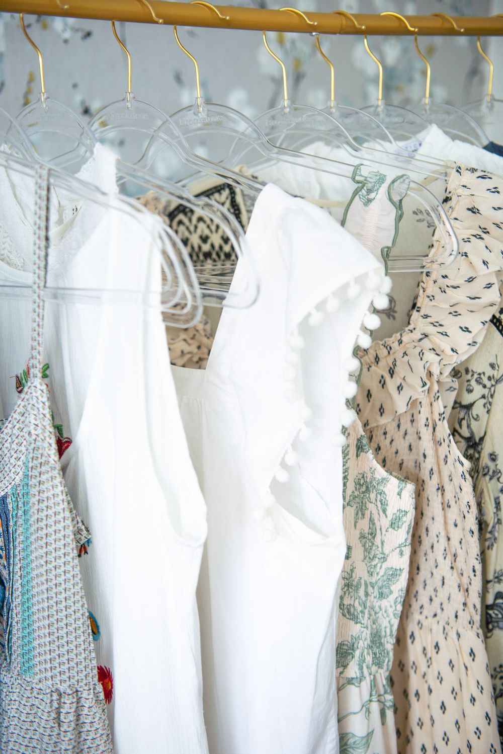 Clean white and patterned baby clothes hang neatly on a clothing rack at a boutique store.