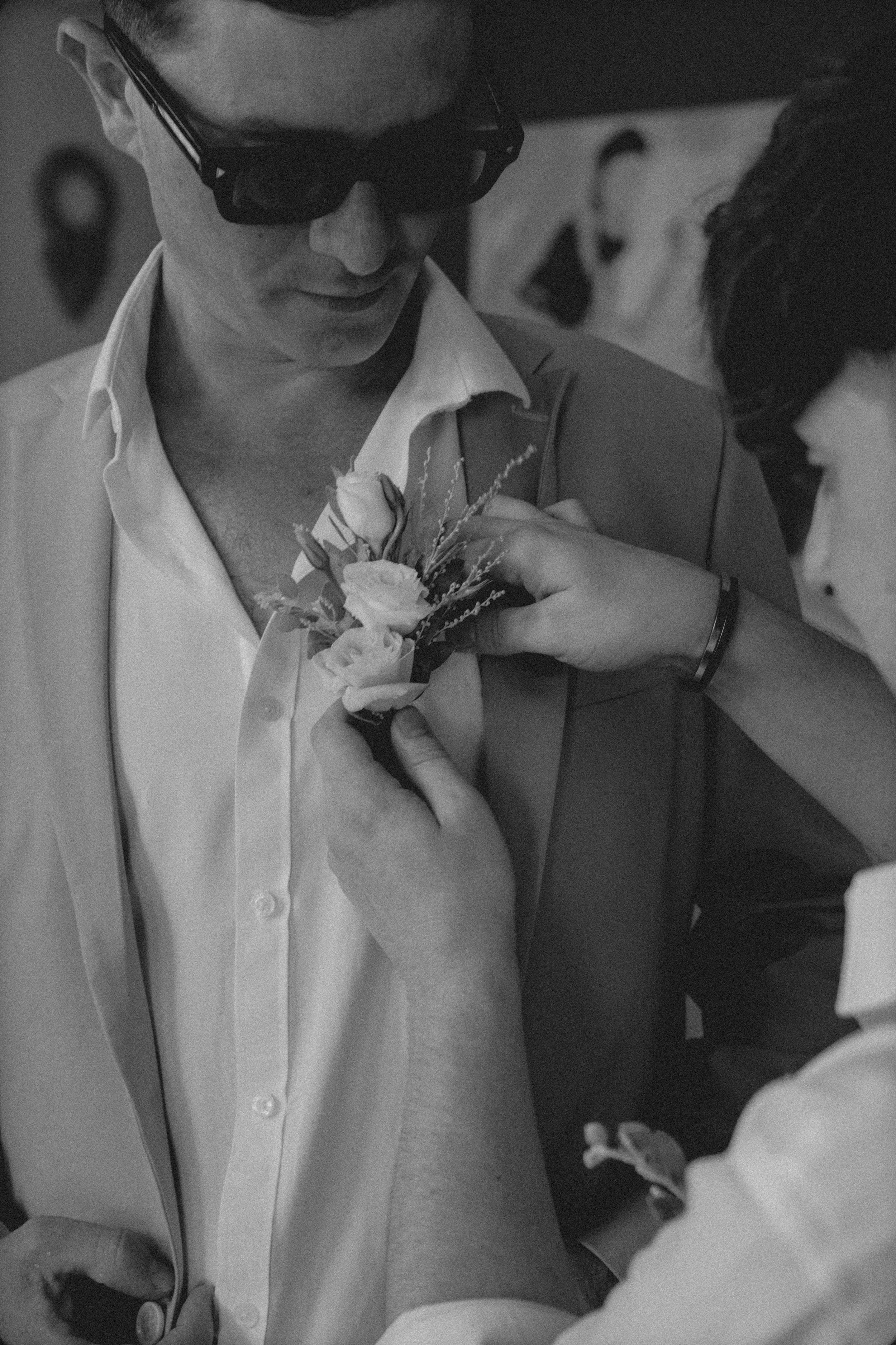 A boutonniere being pinned onto a groom's lapel at a formal event in black and white.