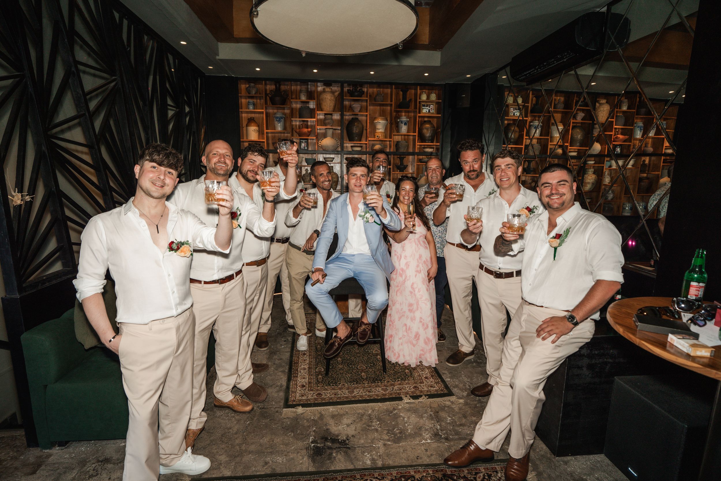 A group of wedding guests wearing white outfits dancing and celebrating at a nighttime reception party.