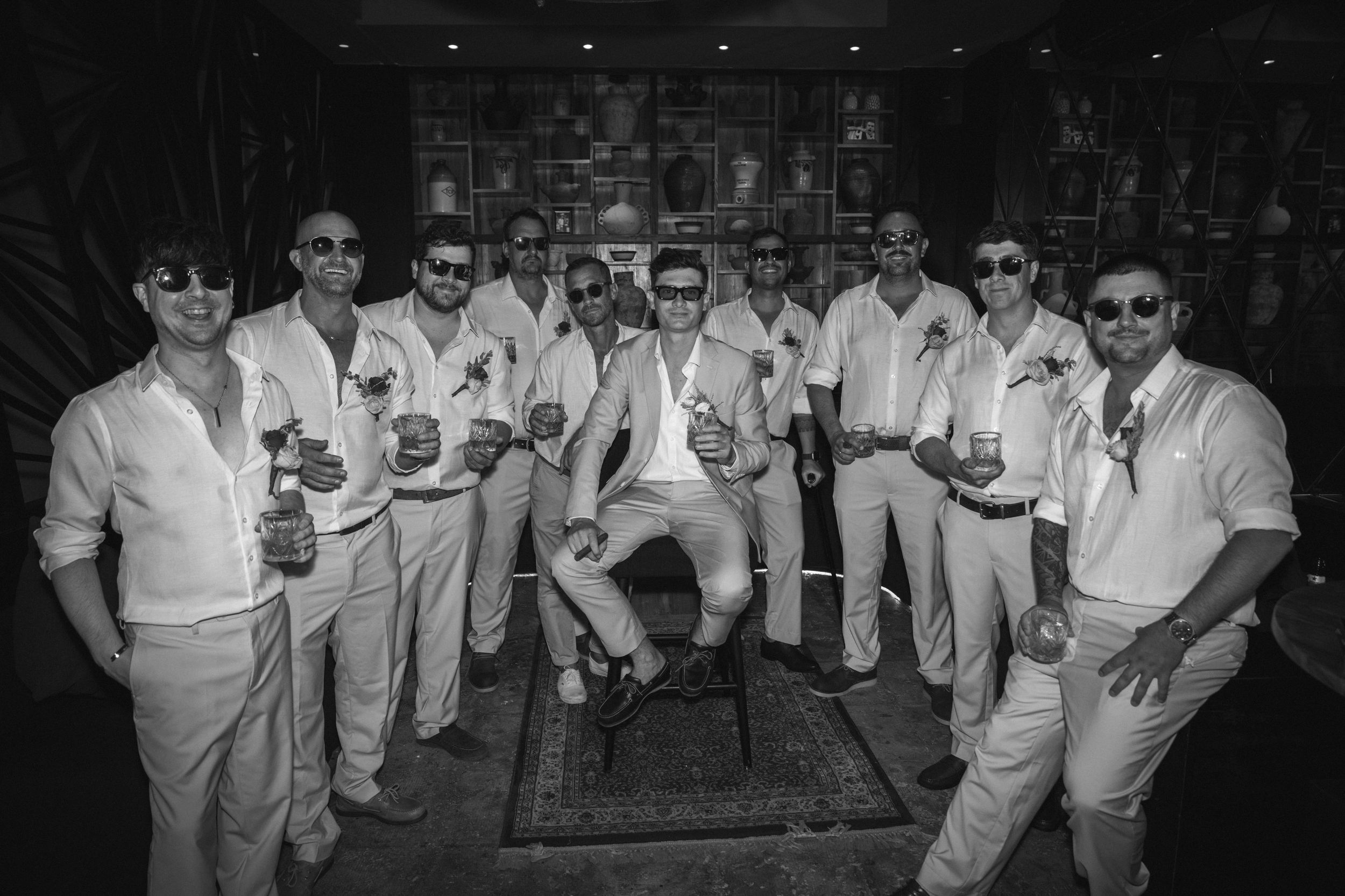 A black and white photo of groomsmen dressed in white suits posing together at a wedding event.