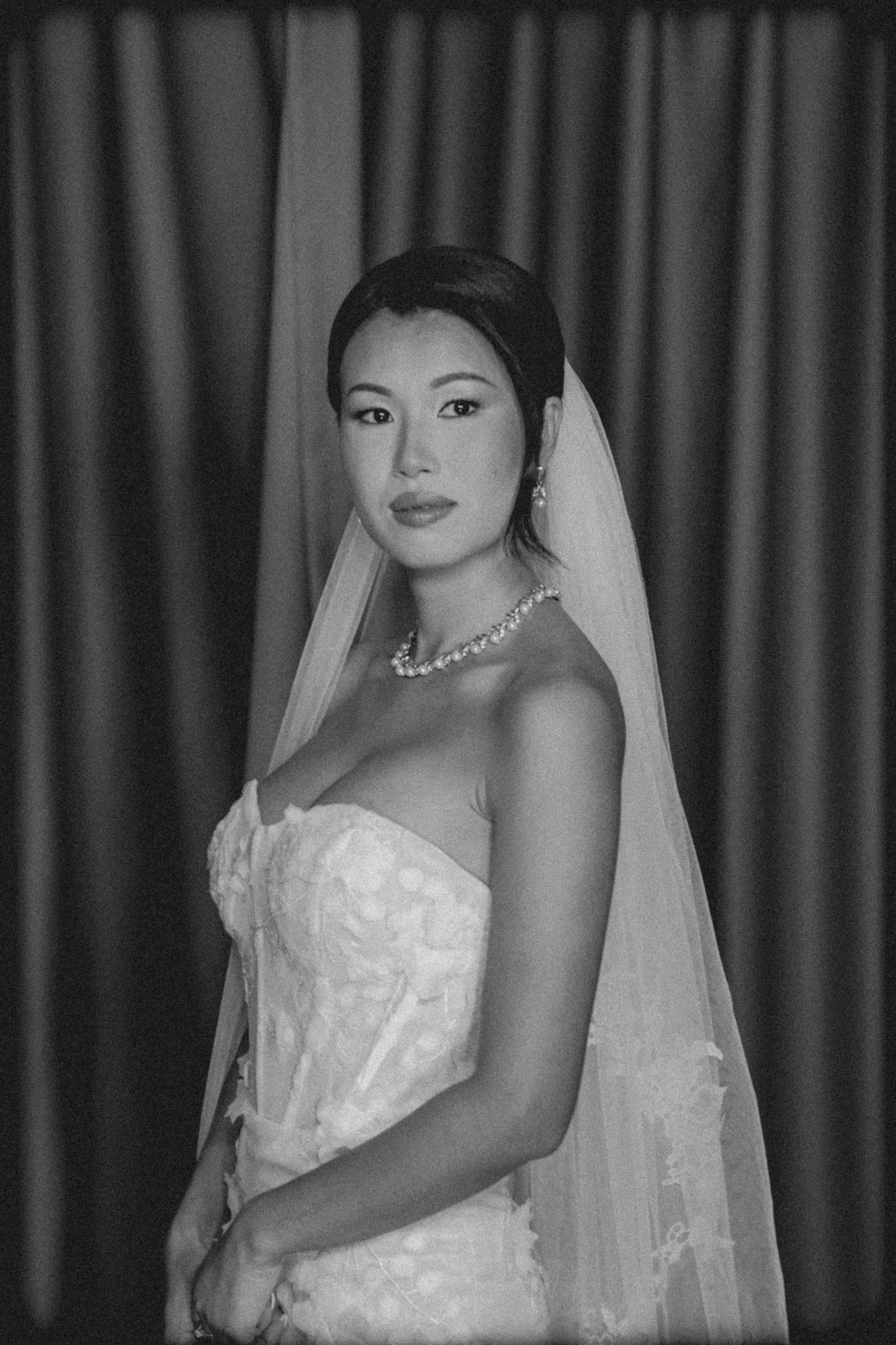 Black and white portrait of a bride wearing a strapless wedding dress, veil and pearl necklace.