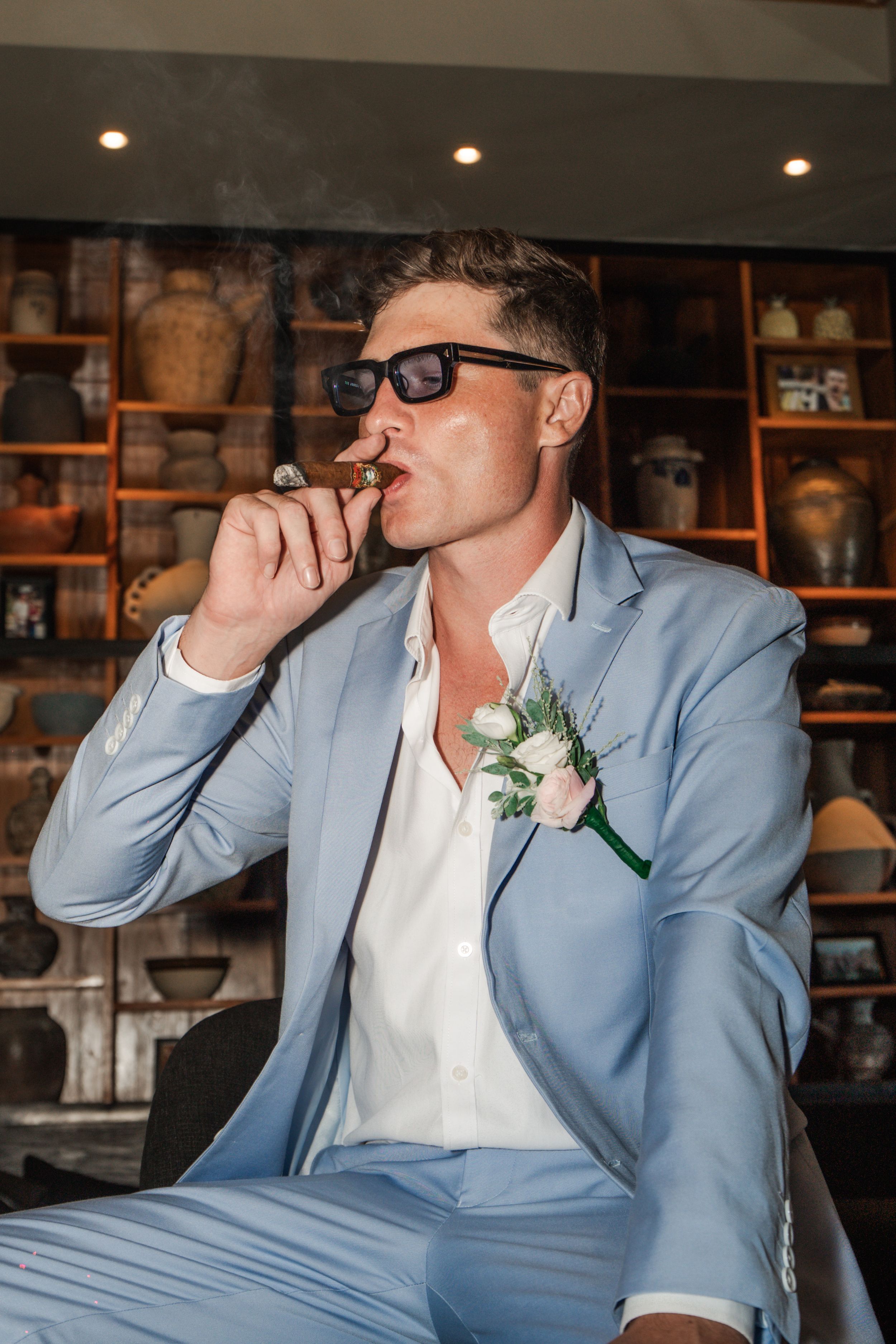 Someone in a light blue suit and white shirt takes shots at a wedding reception venue with wooden decor.