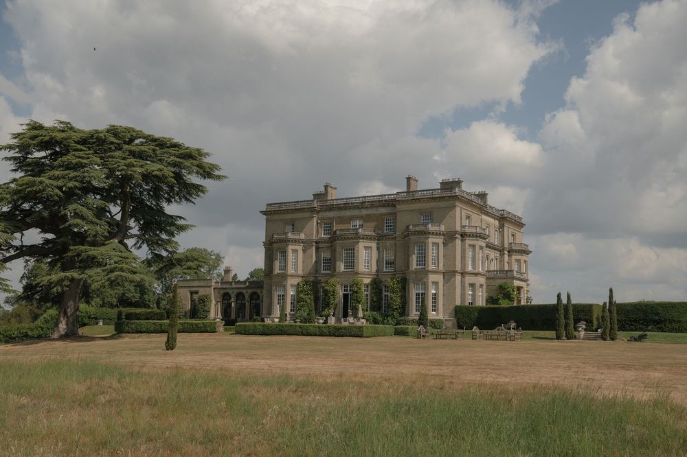 Panoramic view of a stately manor house set against cloudy summer skies.