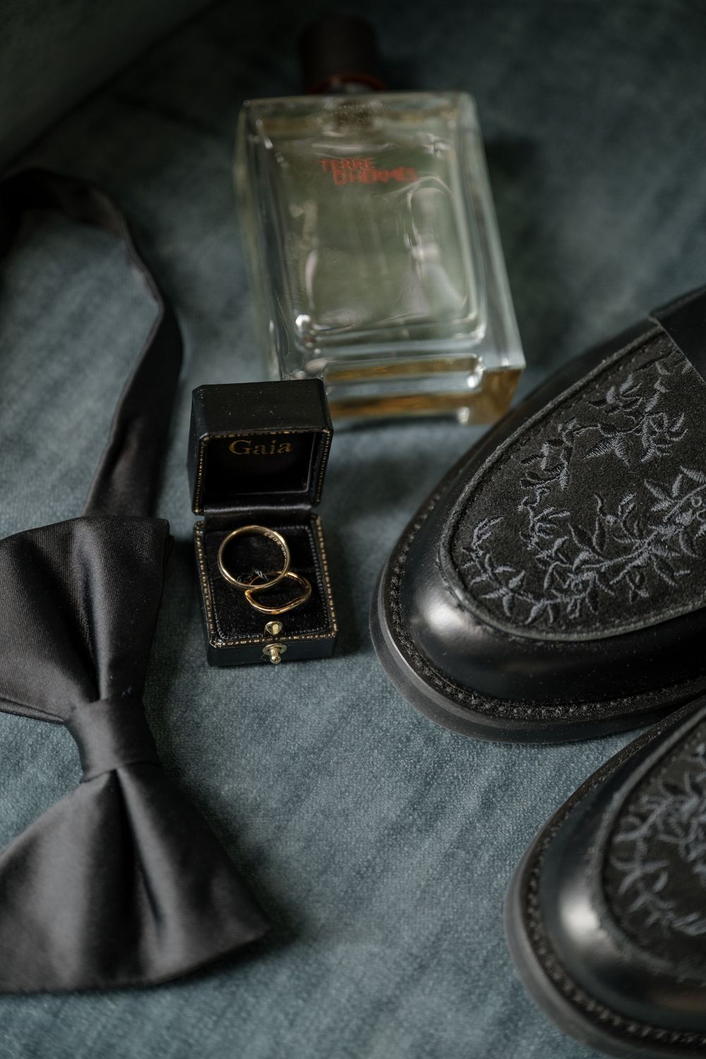 Wedding ring in black box displayed next to formal dress shoes and accessories.