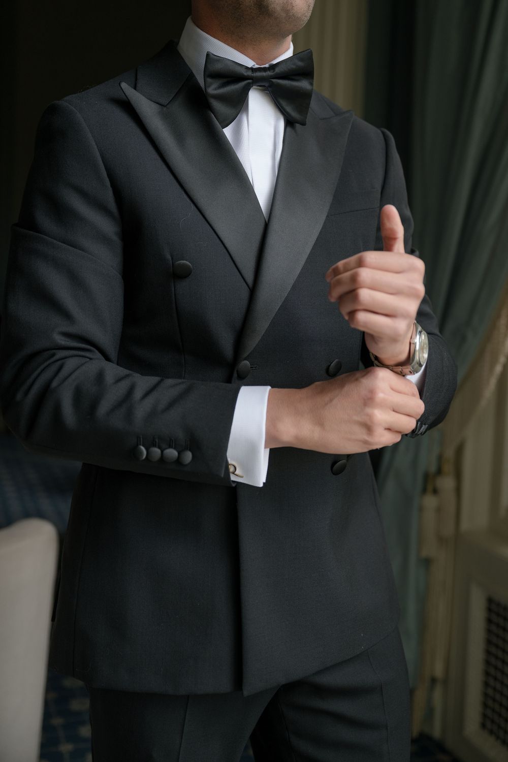 Close-up of groom adjusting cufflink on classic black tuxedo.