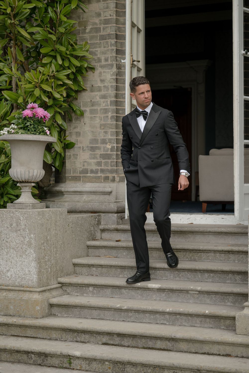 Person in formal tuxedo descending stone steps of historic building.