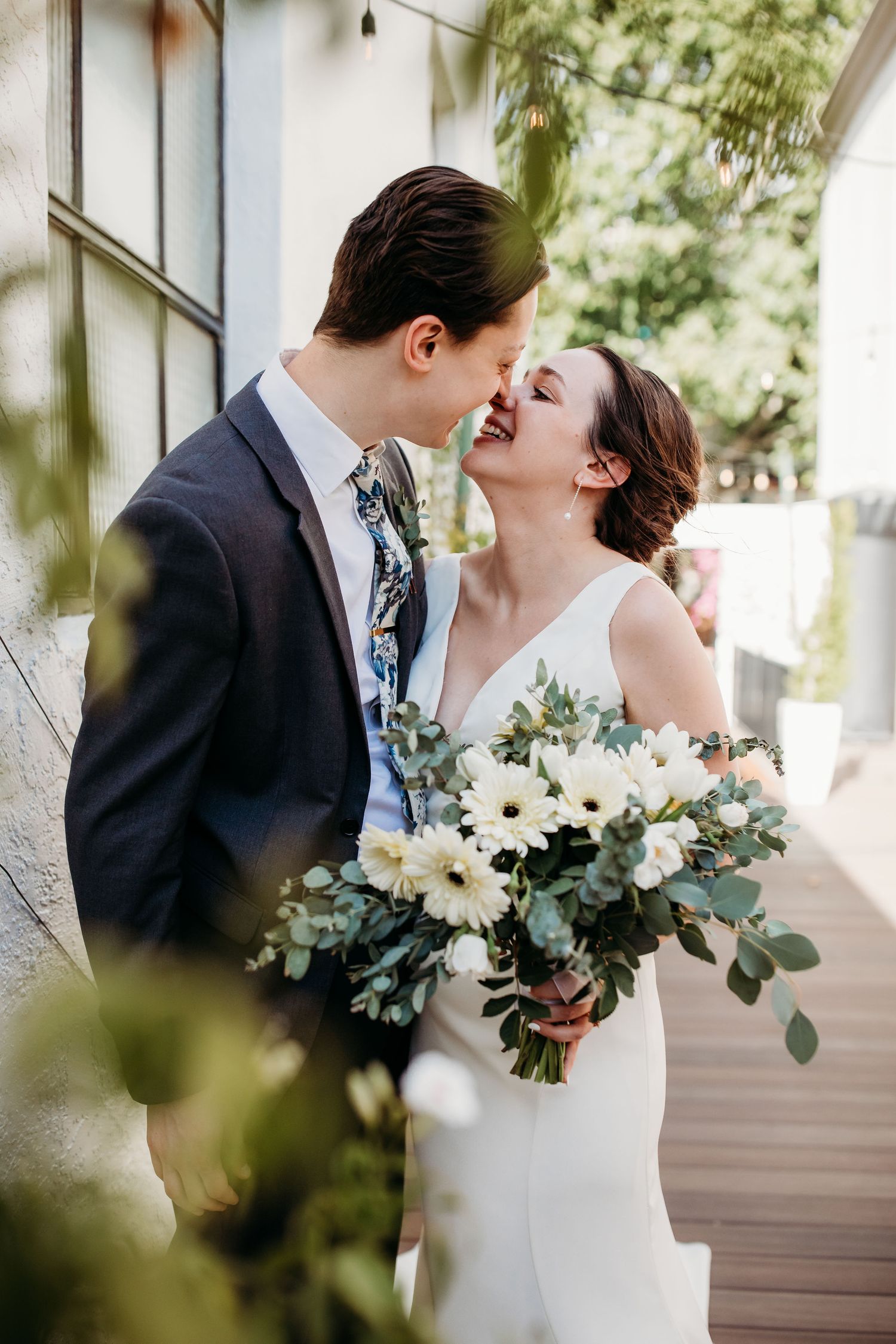 A romantic wedding moment captured outdoors showing a bride in white dress holding a bouquet of white flowers and greenery.