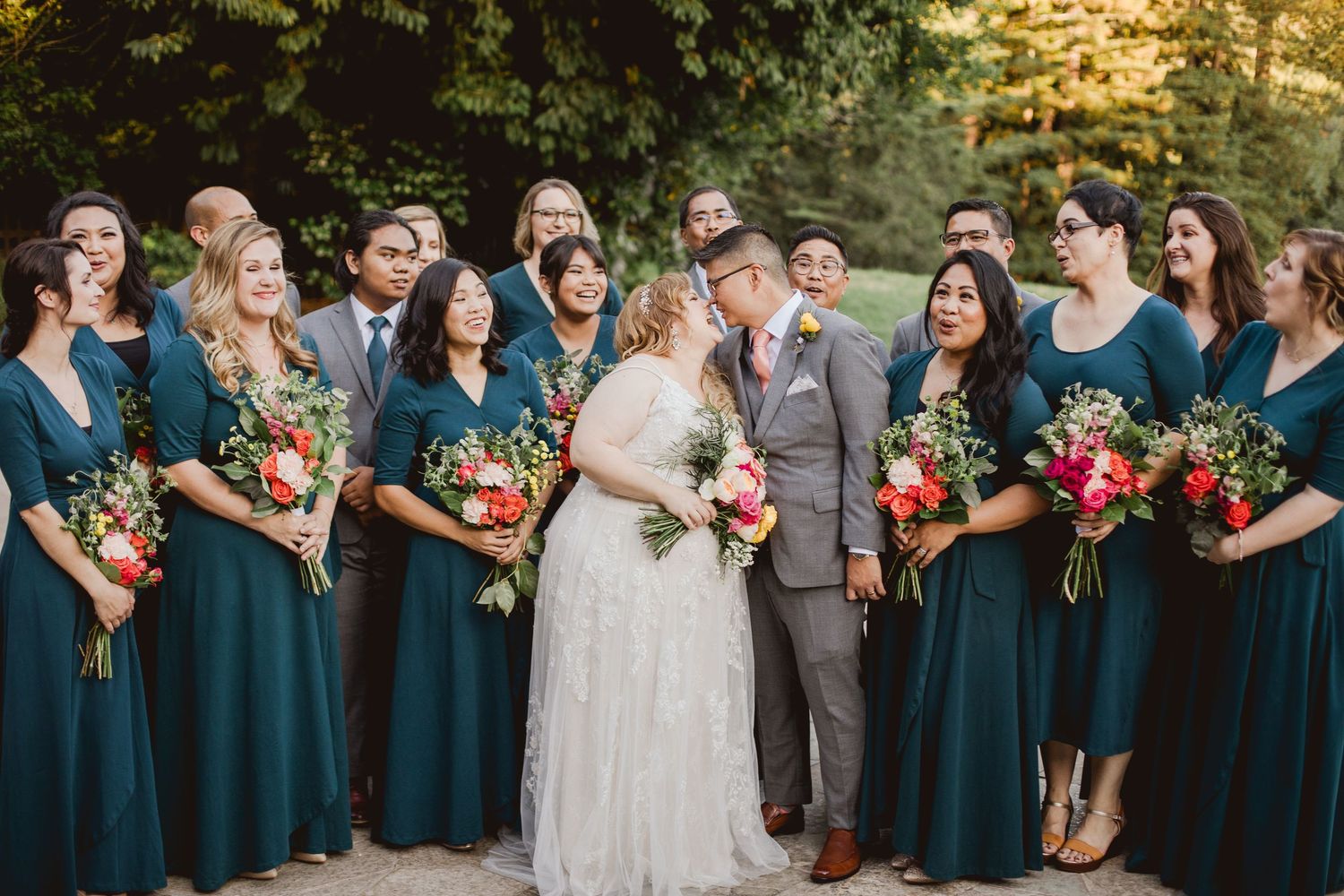 Wedding party holds vibrant fall bouquets while wearing teal dresses and formal attire at an outdoor celebration.