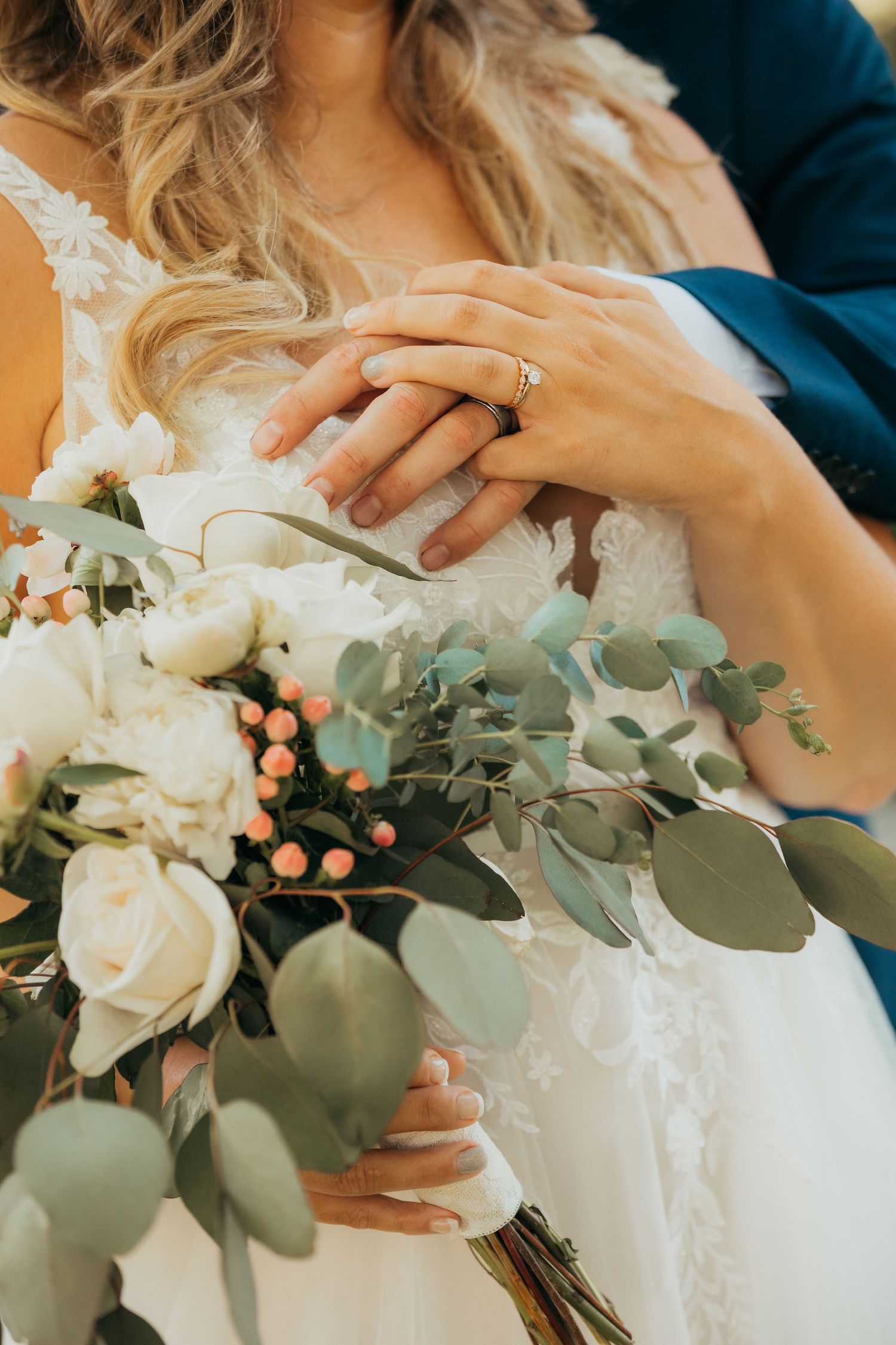 Wedding bouquet details with white roses, eucalyptus leaves and peach berries held against a white dress.
