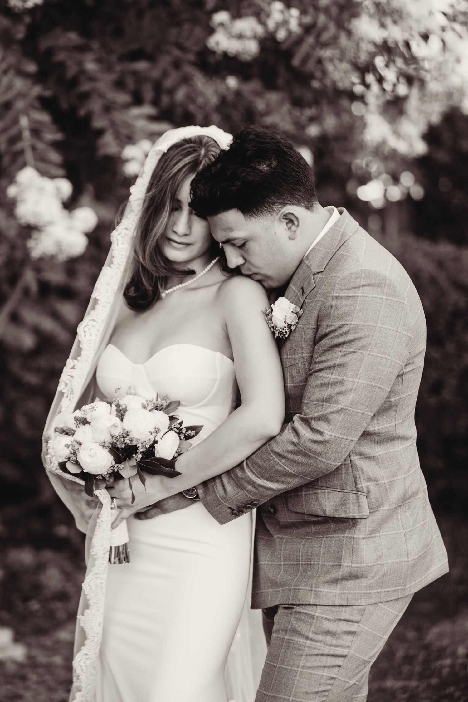 Black and white portrait of a tender wedding moment with the couple embracing while holding a floral bouquet.