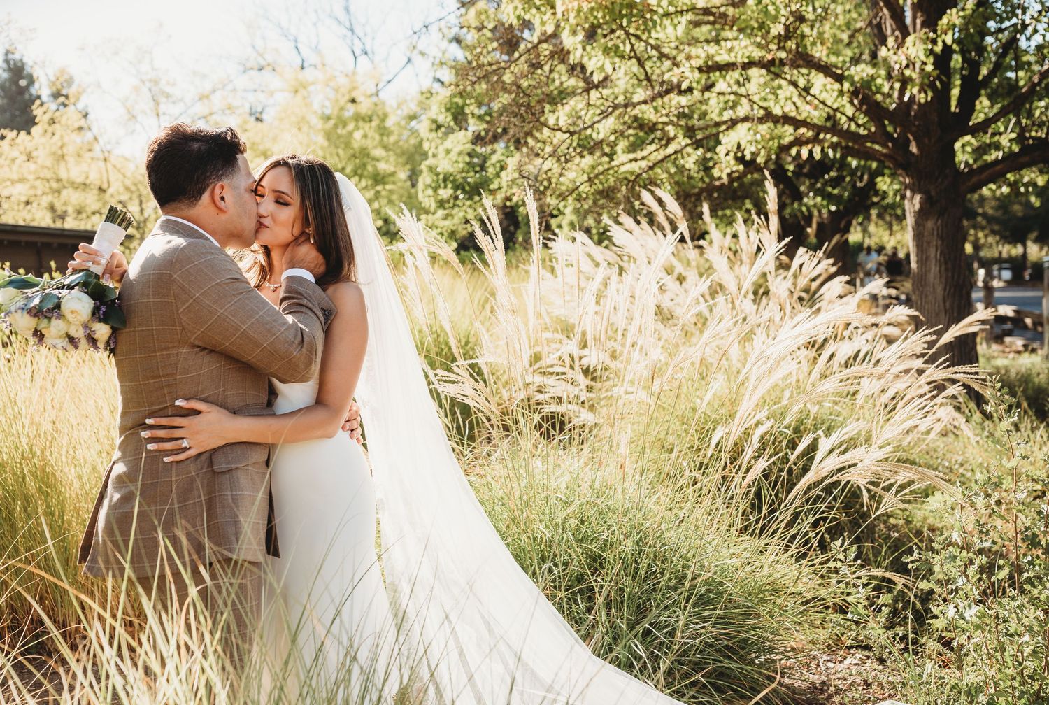 A couple shares intimate moments in golden sunlight surrounded by tall grass and trees during a romantic photoshoot.