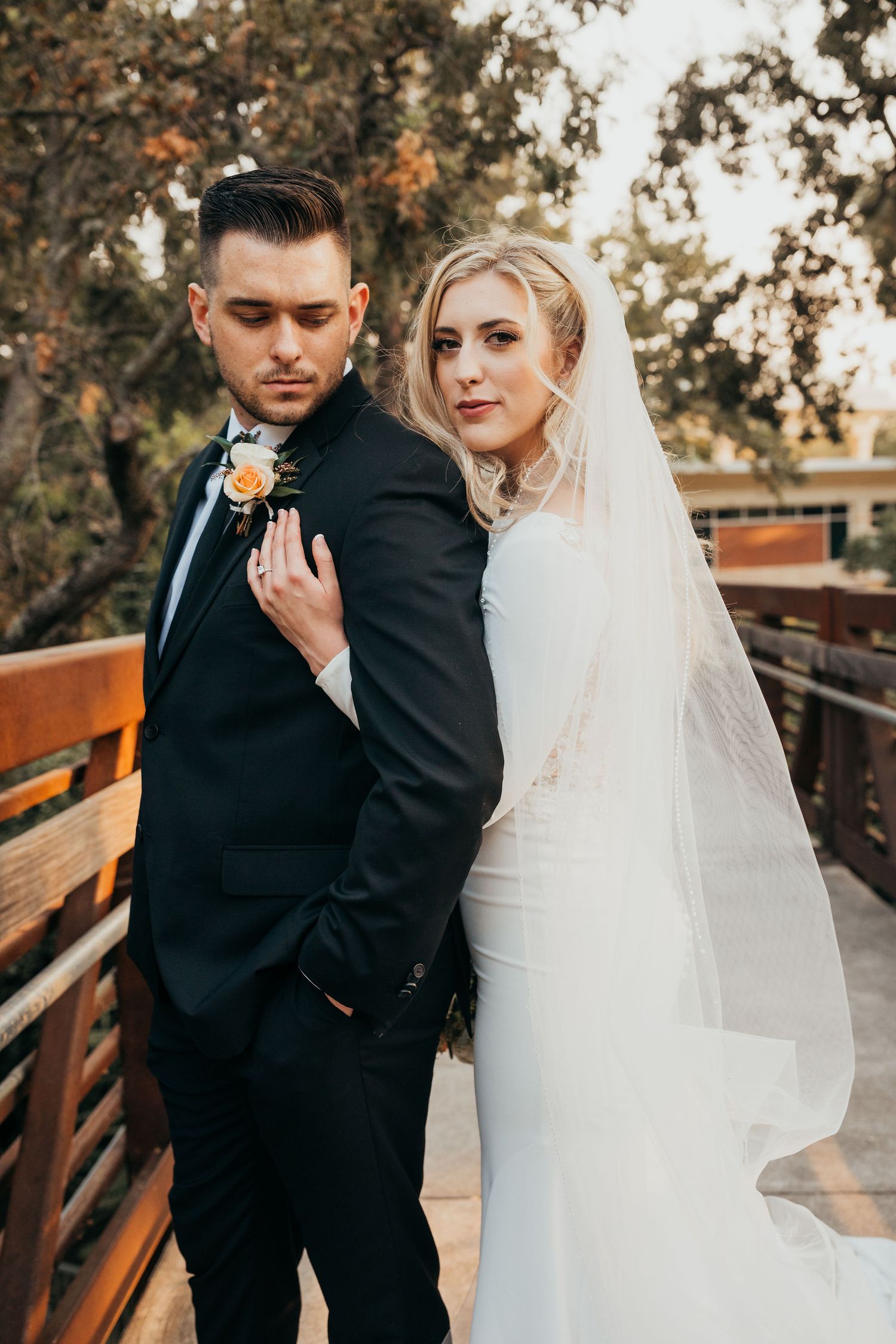 Bride and groom share intimate wedding portraits on a wooden bridge during golden hour beneath autumn trees.