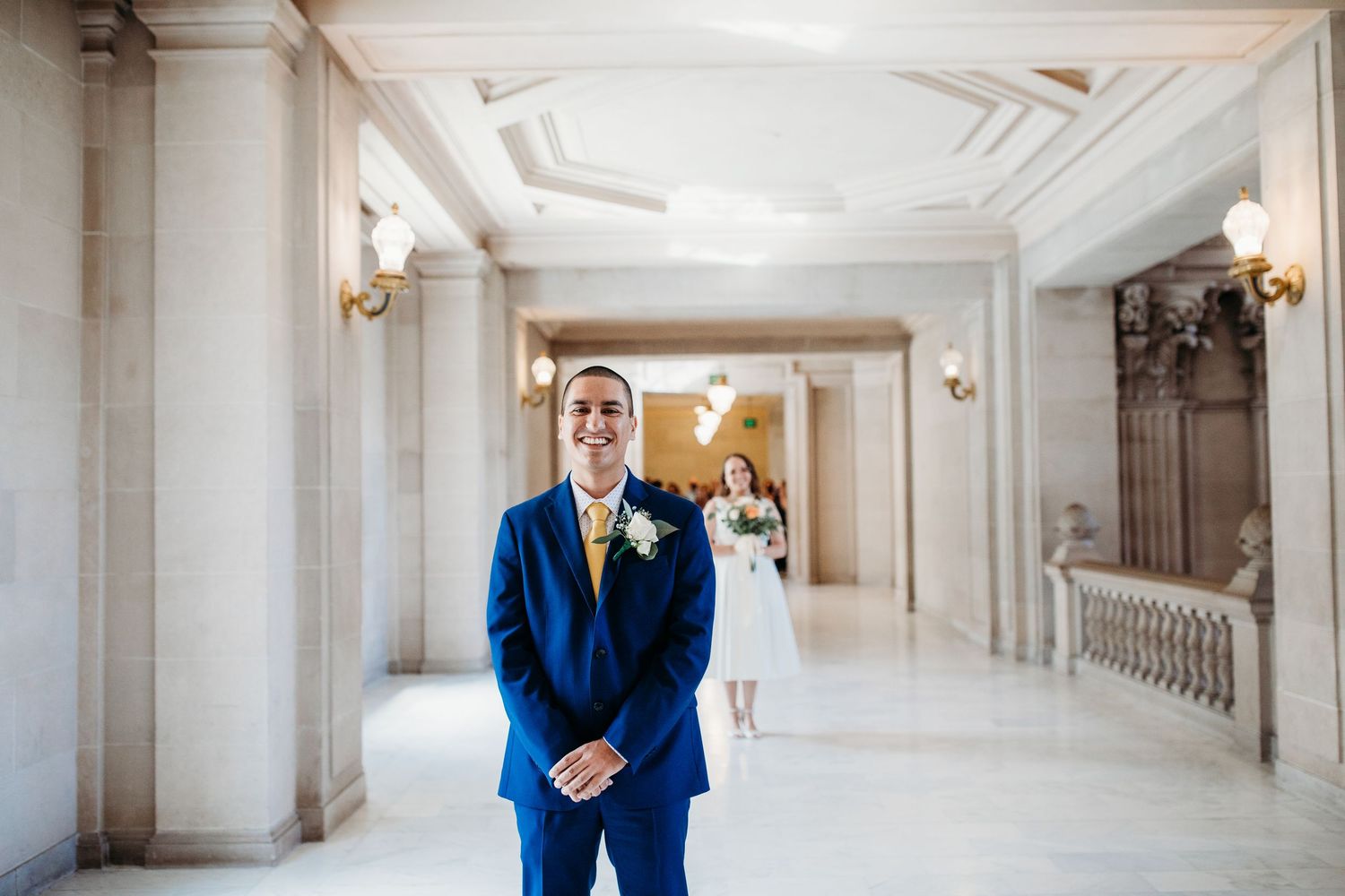 The interior of an elegant white hallway with ornate architectural details and a person in a blue suit standing by a wall.