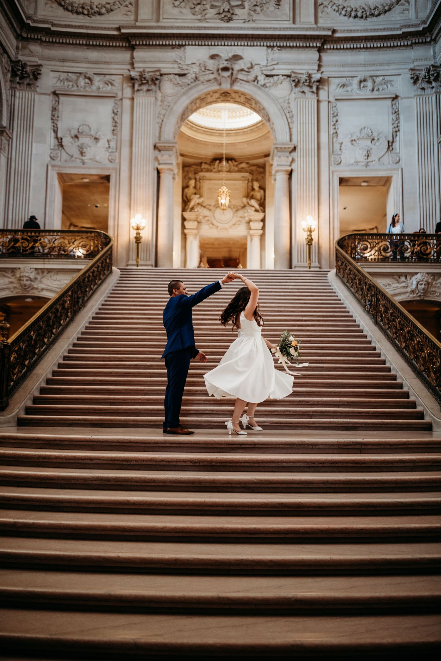 Two figures dance on the grand marble staircase of San Francisco City Hall beneath ornate Beaux-Arts architecture.