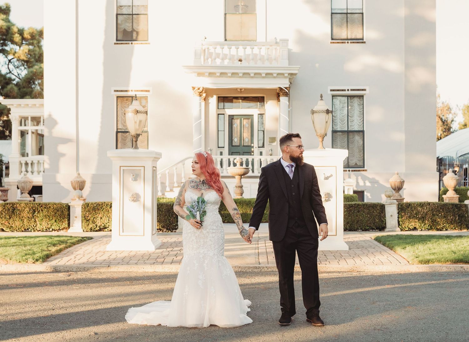 A newly married couple poses together outside a grand white colonial-style building during golden hour.