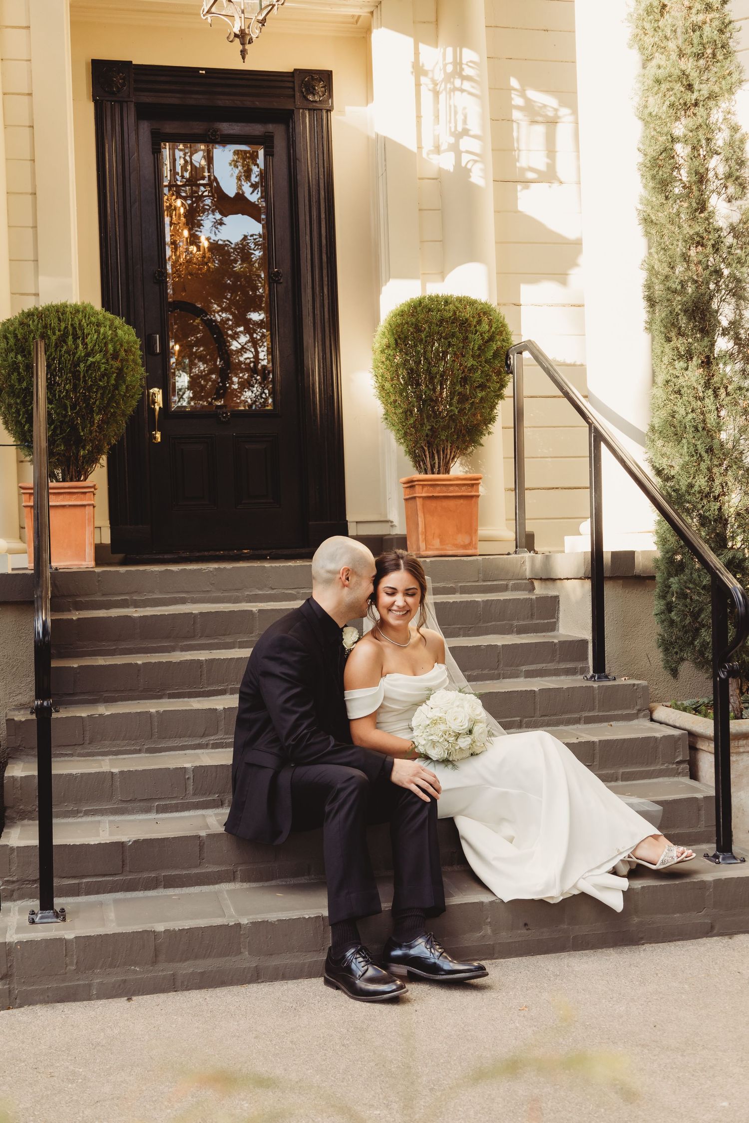 A series of four connected photos showing a wedding couple sitting on stone steps outside an elegant building entrance.