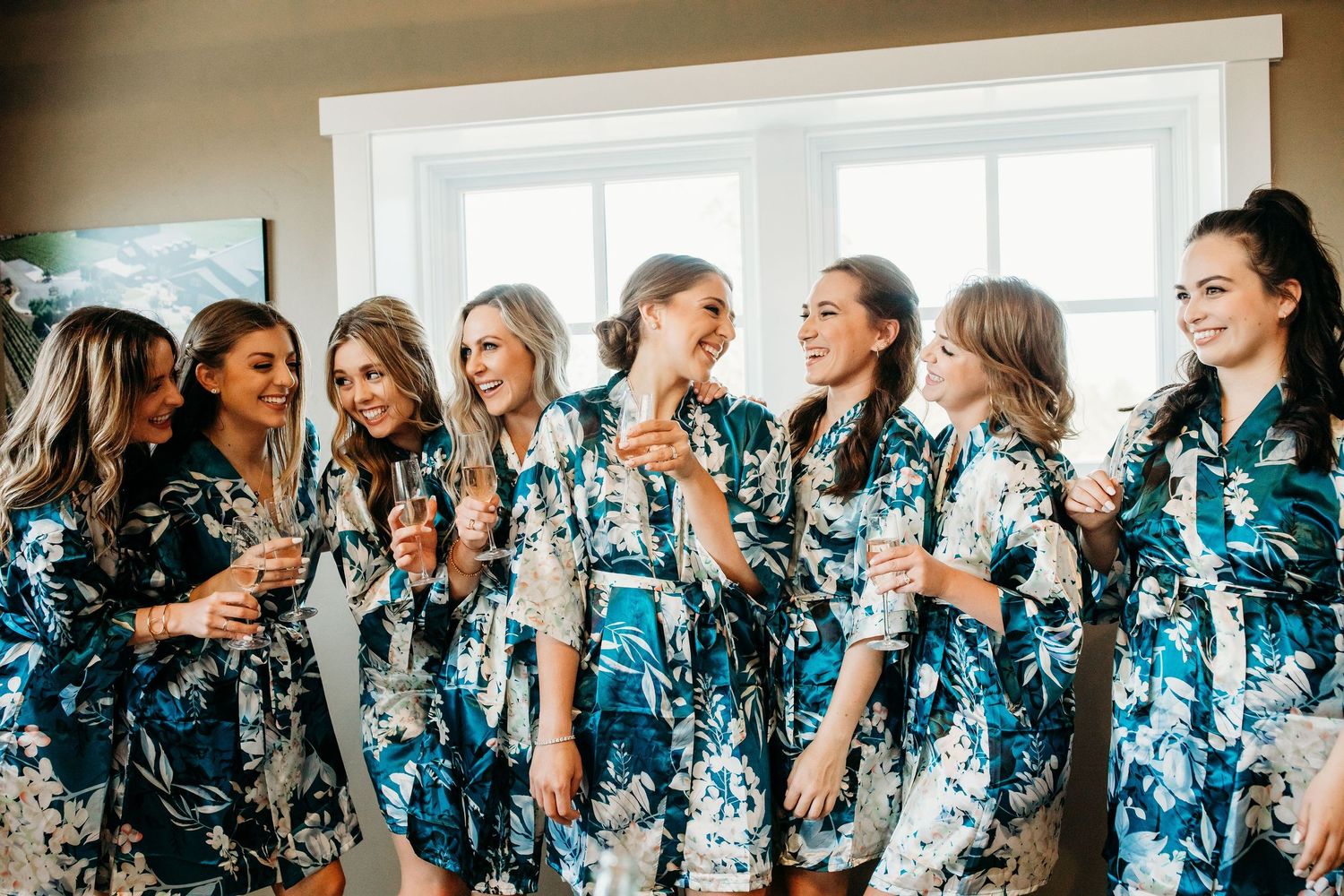 A group wearing matching floral blue robes laughs and talks while standing together in front of windows.