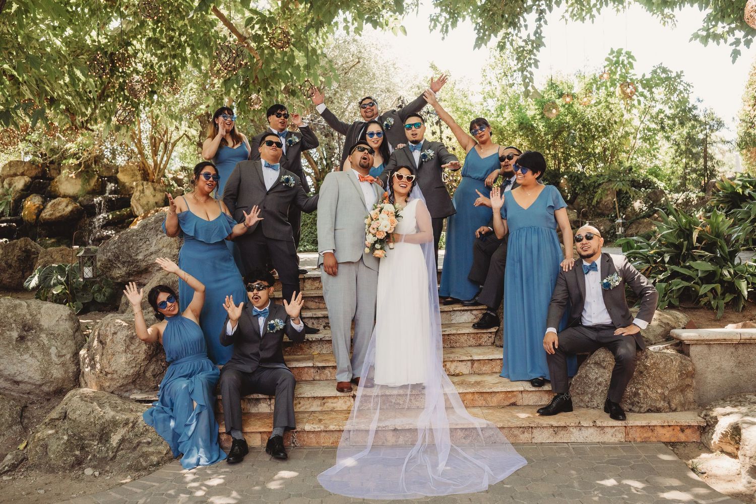 Wedding party celebrating outdoors in coordinated blue attire under trees.