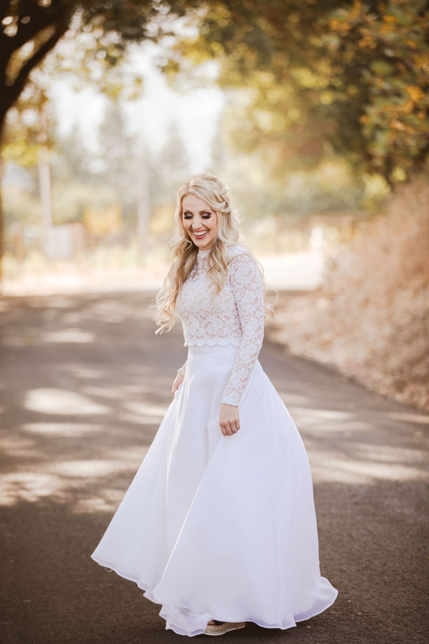 A wedding photoshoot on a sunlit path captures a flowing white lace gown twirling in the golden afternoon light.