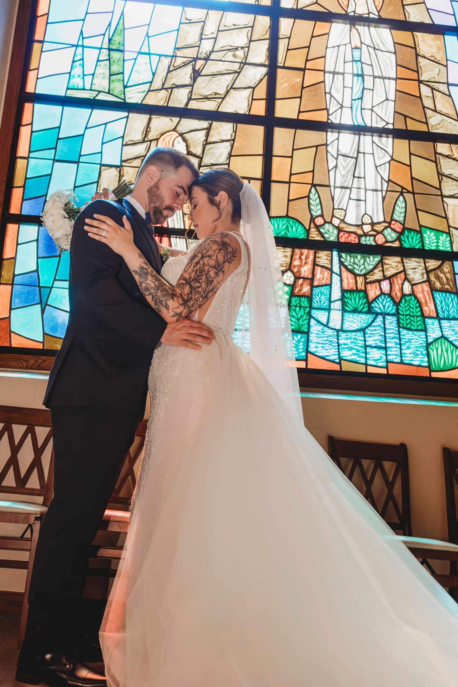 A bride and groom share an intimate moment in front of a beautiful stained glass window in a church.