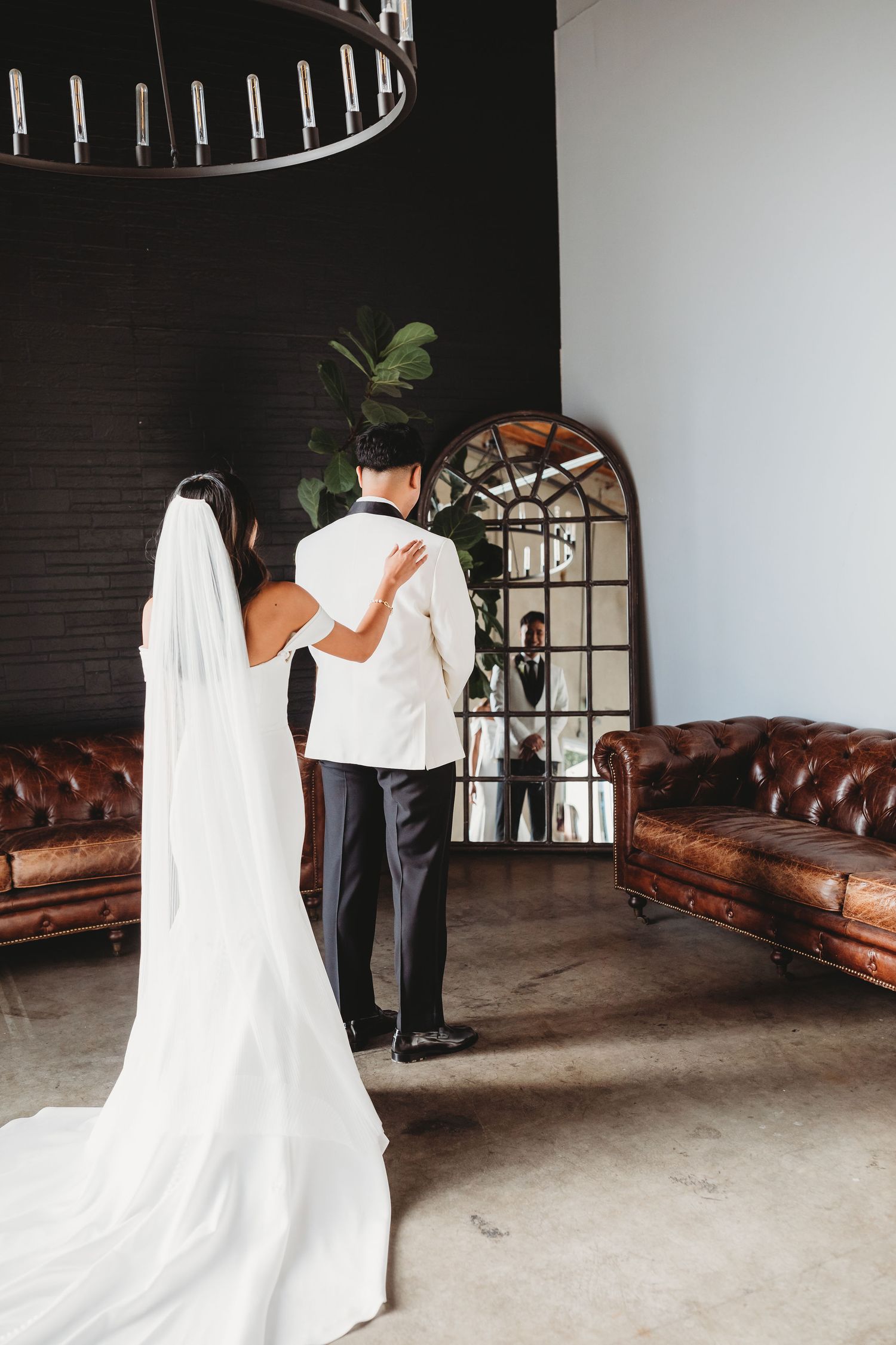 Ghost-like figure in flowing white fabric follows dark-dressed person through modern interior space near leather couch.
