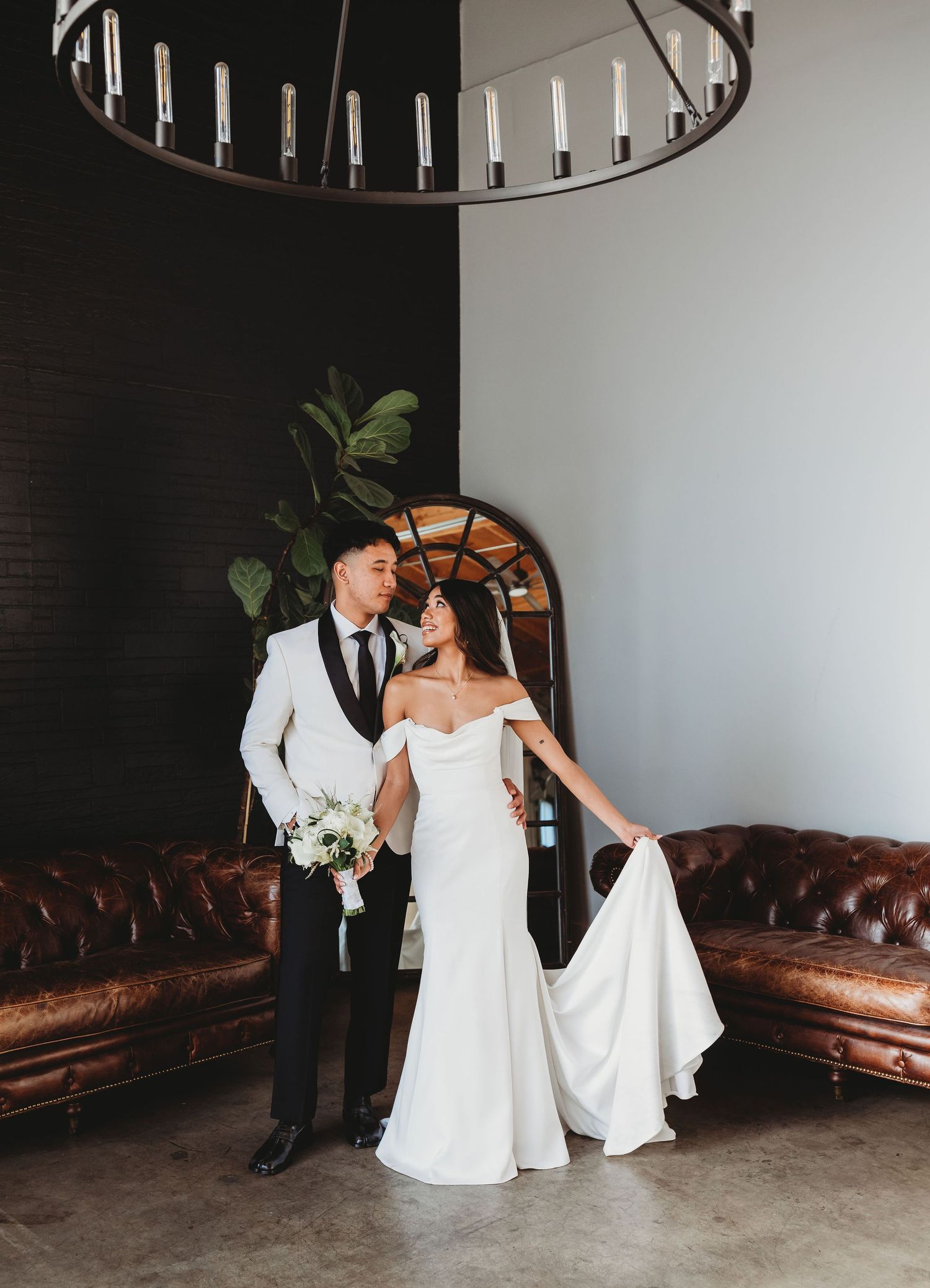 A couple in wedding attire dances and twirls together in an industrial venue with exposed walls and leather sofas.