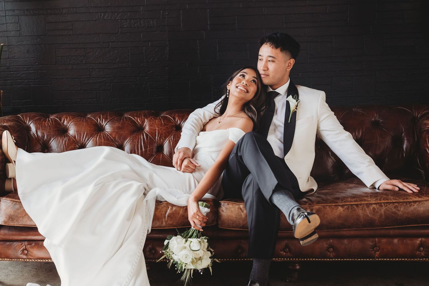 A romantic wedding photo series showing a couple lounging together on a brown leather couch in various playful poses.