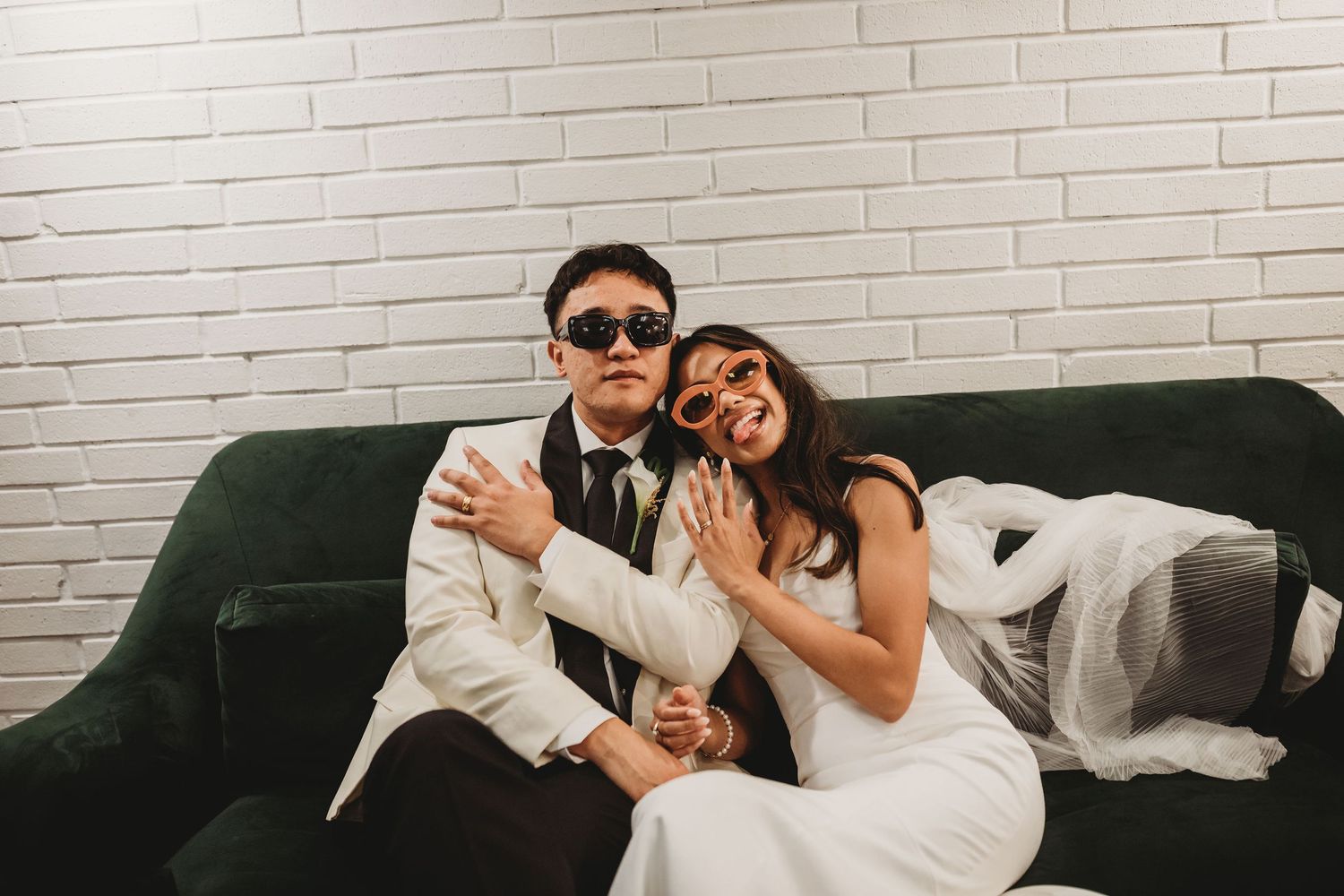 Wedding couple relaxing and smiling together on dark green velvet couch at photo session.