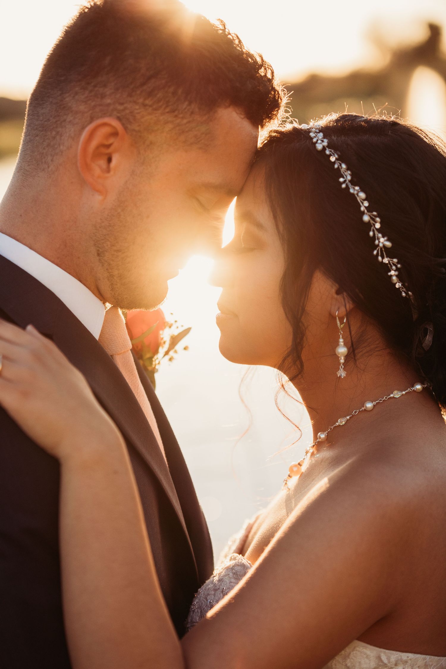 A romantic couple shares an intimate moment at sunset while backlit by golden sunlight in their wedding attire.