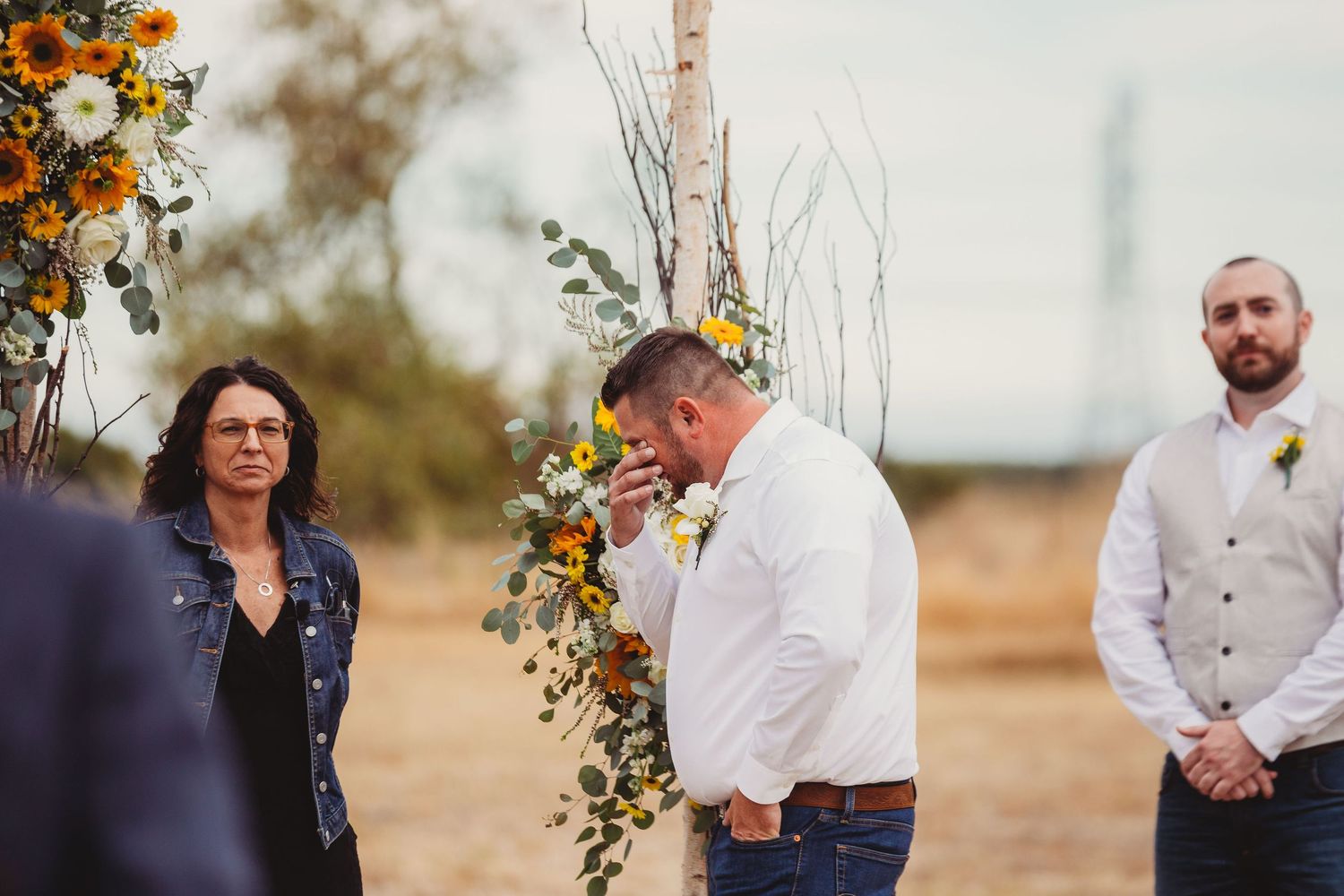 A group gathers in a golden hour outdoor ceremony setting with orange floral arrangements and natural desert landscape.
