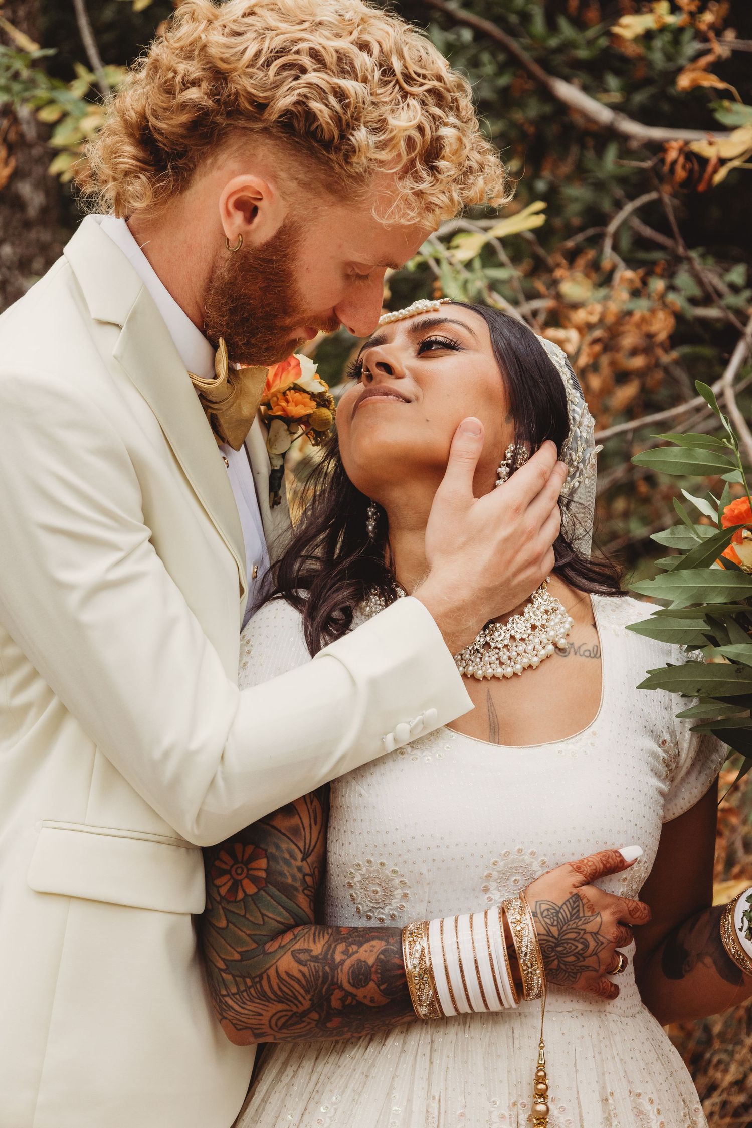 A romantic wedding couple in white attire share intimate moments surrounded by autumn foliage.