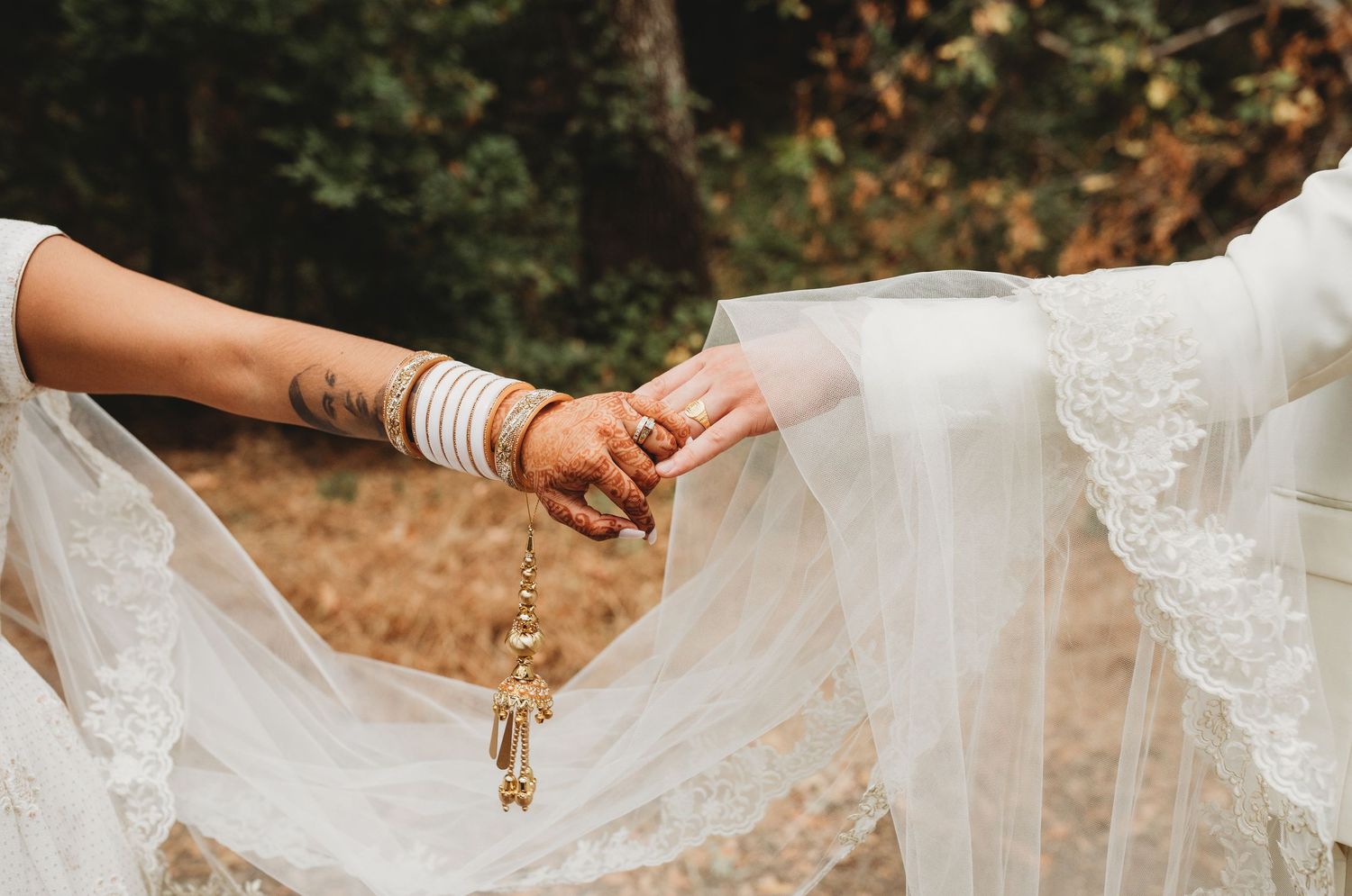 Two hands hold onto each other against a backdrop of white lace wedding dress fabric in an outdoor setting.