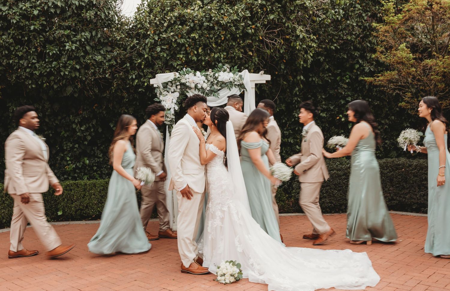 Wedding party poses playfully on a brick pathway surrounded by autumn foliage.