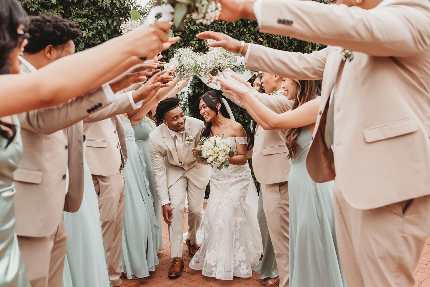 Wedding party forms a tunnel for the newlyweds to walk through during outdoor celebration in pastel attire.