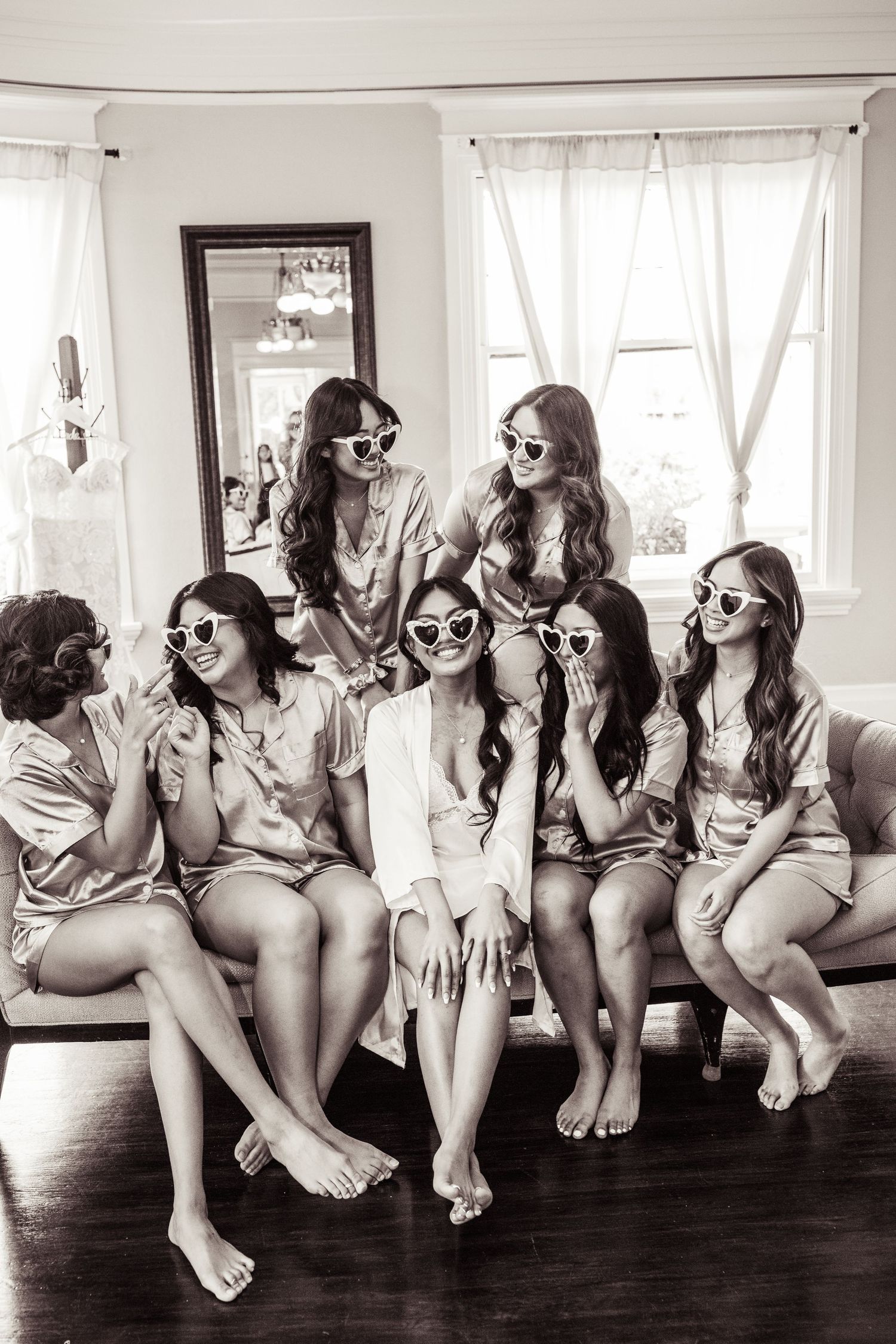 A black and white image of bridesmaids wearing sunglasses sitting in a row during a wedding photoshoot.