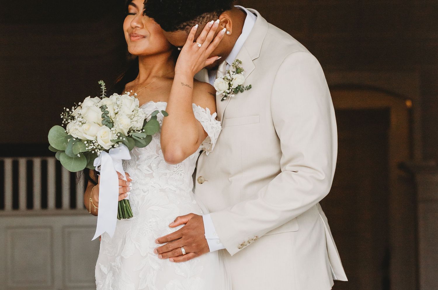 Romantic wedding couple embrace in formal attire against a blurred background.