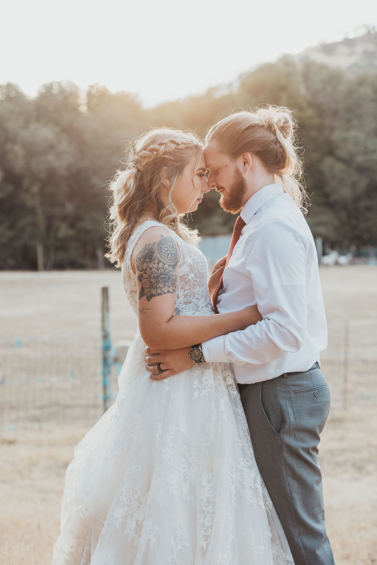 A romantic sunset wedding portrait shows a couple in delicate embrace wearing white dress and formal attire outdoors.