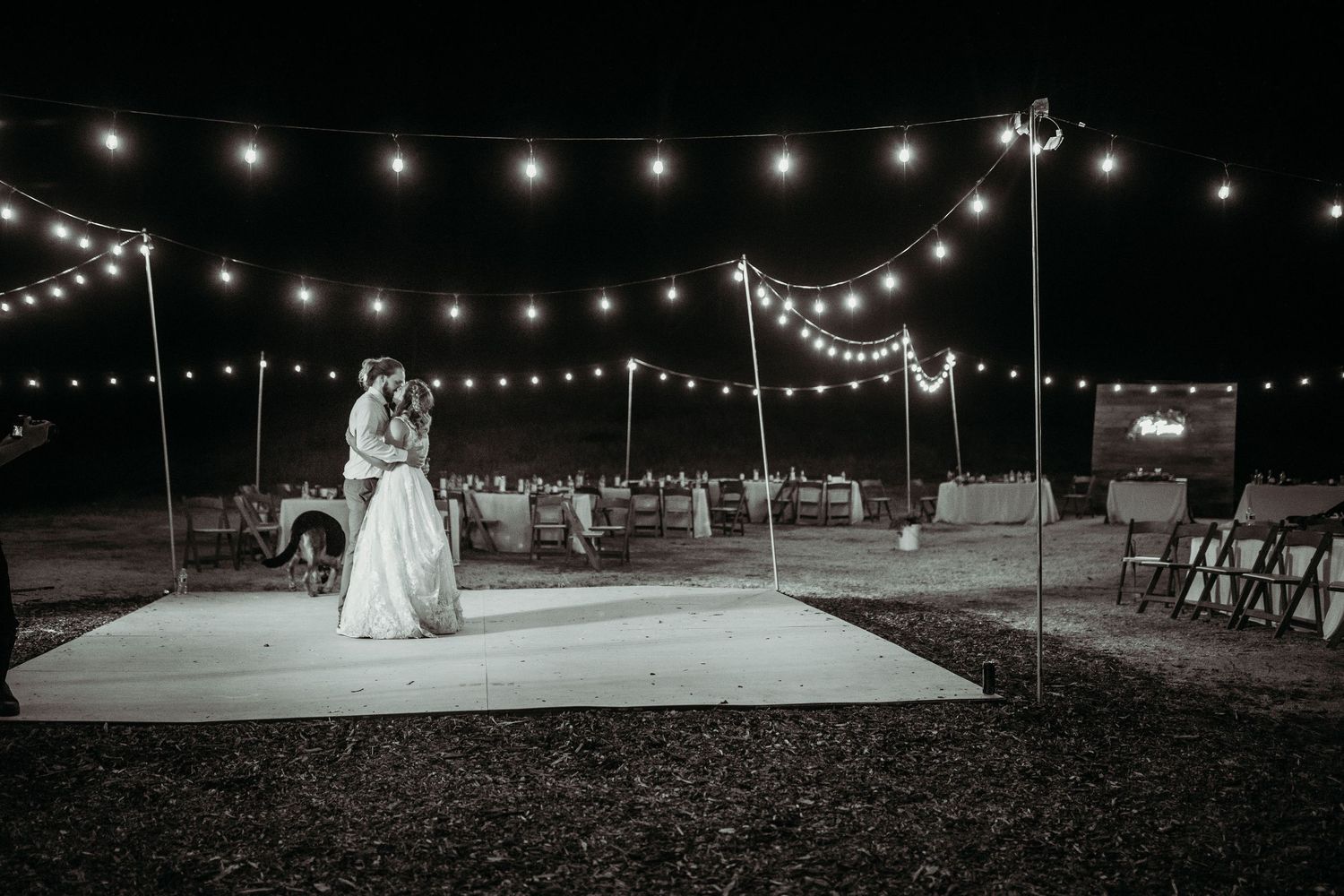 A romantic evening dance beneath string lights on an outdoor dance floor during a nighttime celebration.