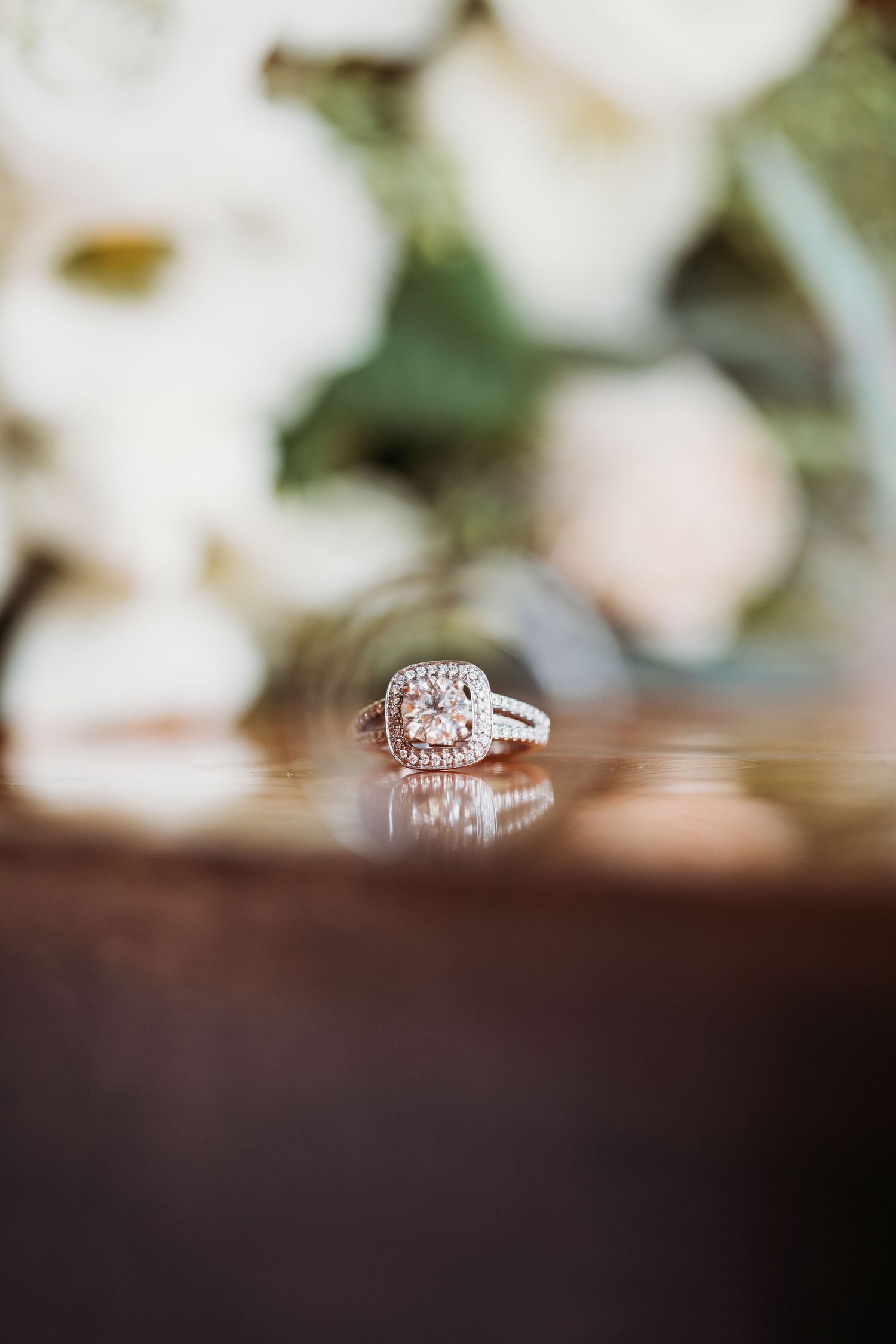 Elegant diamond engagement ring with cushion cut center stone and halo setting reflected on dark wooden surface.