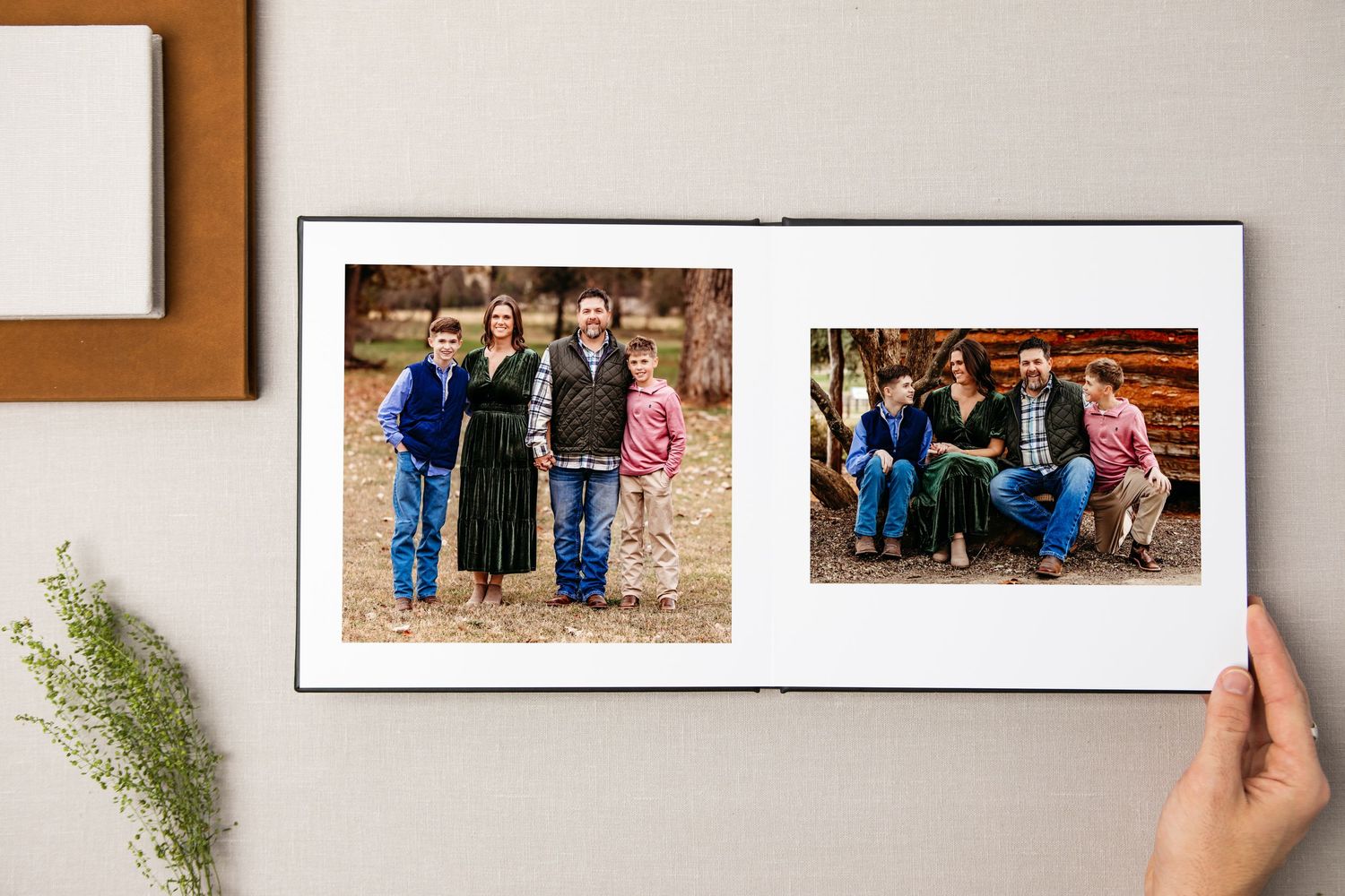 Hands hold open a photo album displaying two family portrait photographs on a wooden surface with greenery in Grapevine, TX