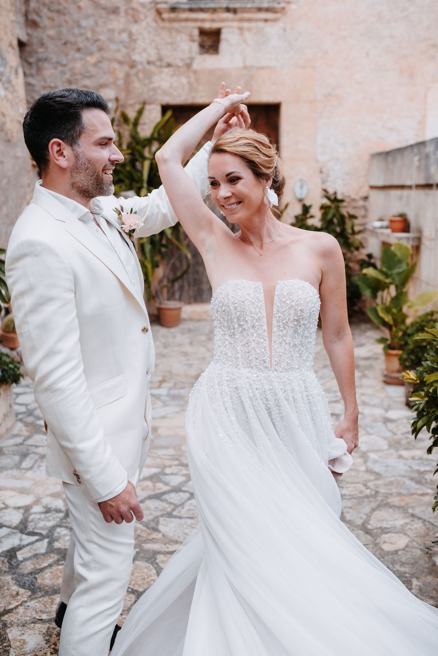 Eine romantische Tanzsequenz in weißer Hochzeitskleidung vor einer rustikalen Steinmauer als Hintergrund, in der Finca Xiclati auf Mallorca.